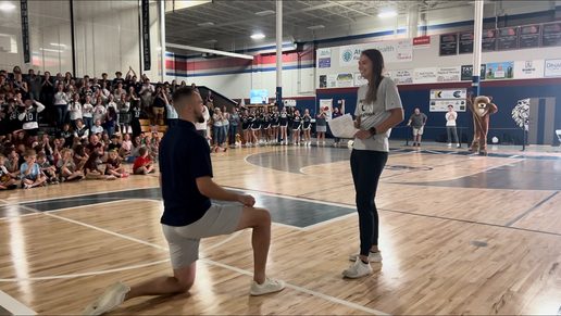 Coach Davy Fisher on one knee in the gym during the pep rally