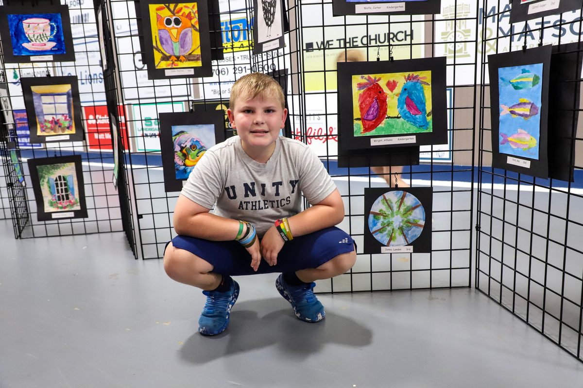 A student crouching beside a wall of framed student artwork