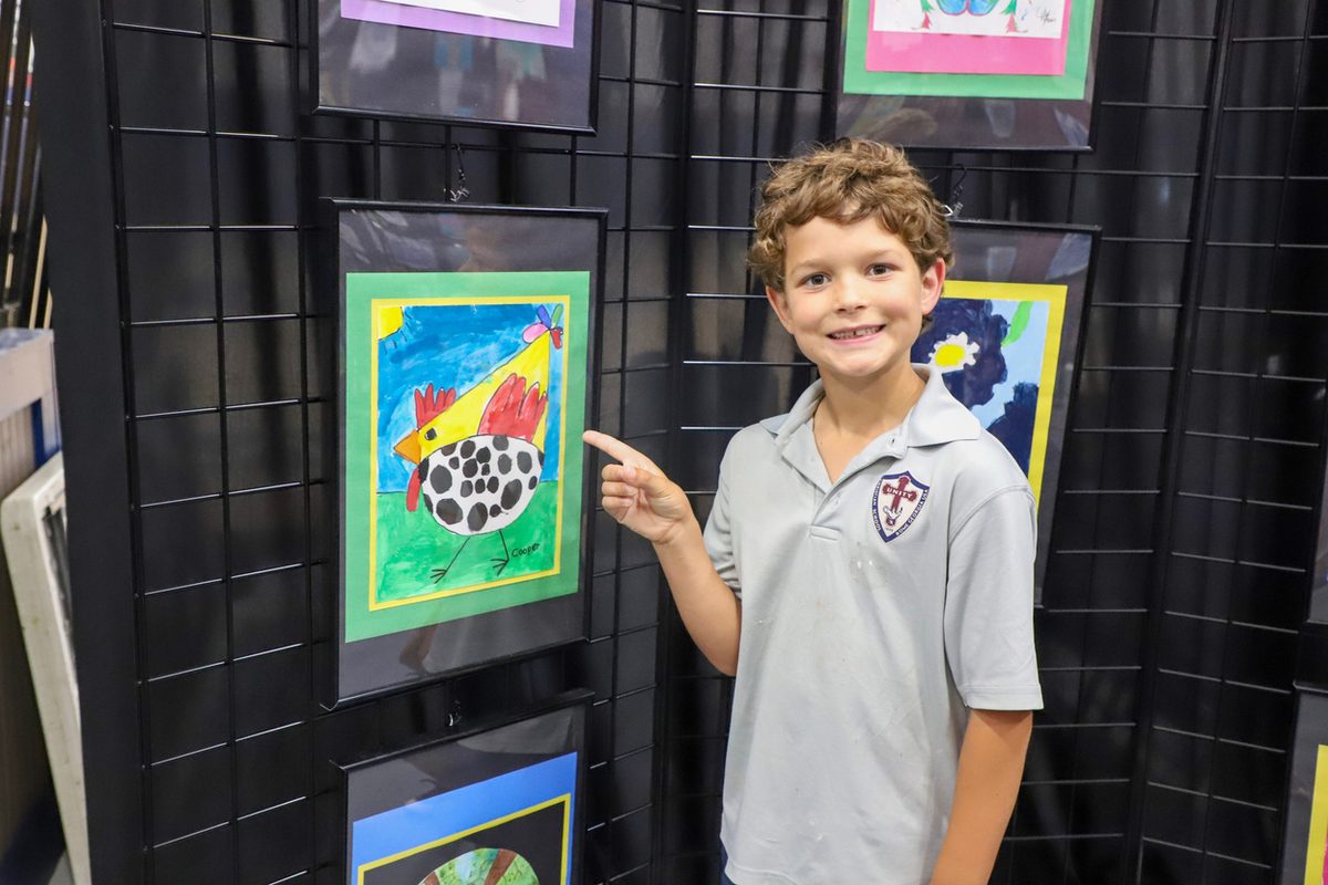 A student pointing out his painting on the display grid